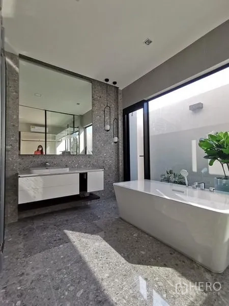 Detached House for rent or sale in Saphan Sung, Bangkok - Sunlit bathroom with freestanding tub, large mirror and sliding glass door to a small courtyard.