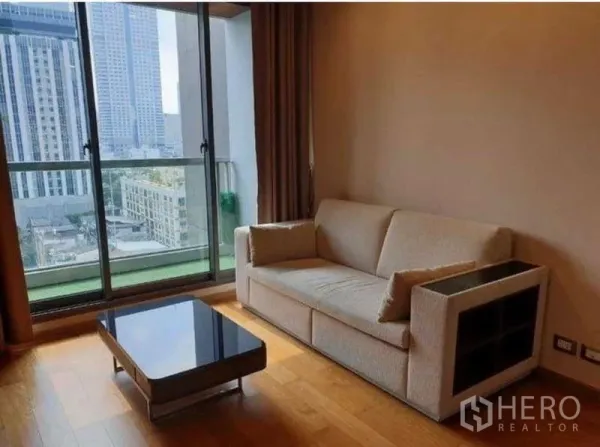 公寓 出租在Bang Rak, Bangkok - 客厅采光充足，米色沙发与玻璃茶几，落地推拉门连通阳台，眺望沙吞天际线。