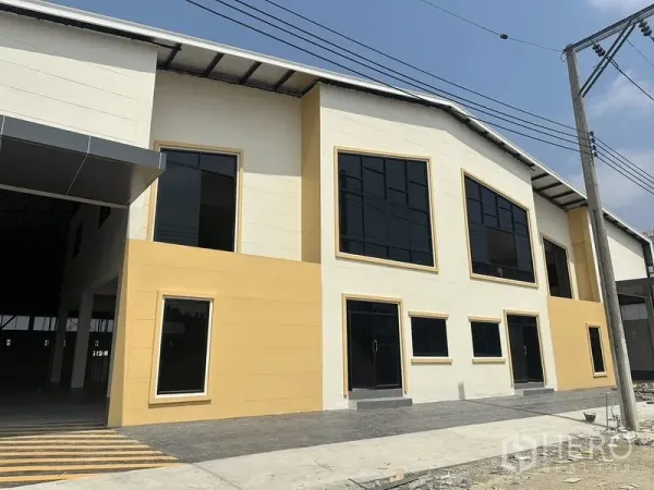 货栈 出租在Bang Pakong, Chachoengsao - 新建仓库正立面，深色玻璃窗，铺装前场及带顶装卸区。