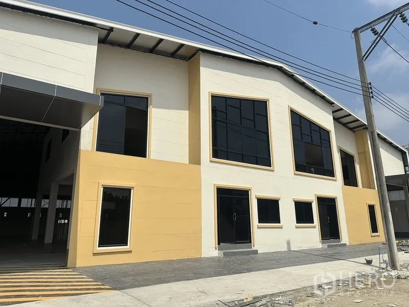 货栈 出租在Bang Pakong, Chachoengsao - 新建仓库正立面，深色玻璃窗，铺装前场及带顶装卸区。