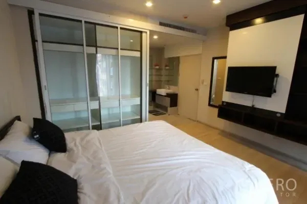 Condominium for rent in Watthana, Bangkok - Primary bedroom with sliding‑door wardrobe, wall‑mounted TV and ensuite vanity.