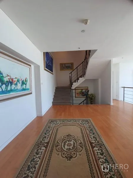 公寓 出售在Watthana, Bangkok - 宽阔走廊，浅色木地板与花纹地毯，旁有金属栏杆楼梯。