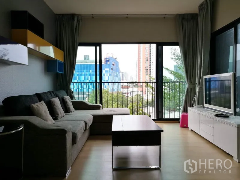 คอนโด ให้เช่าในWatthana, Bangkok - มุมห้องนั่งเล่นอีกด้าน โซฟา ชั้นลอยตกแต่ง ผนังกระจกสูงจรดเพดาน และทิวทัศน์เมืองจากระเบียง