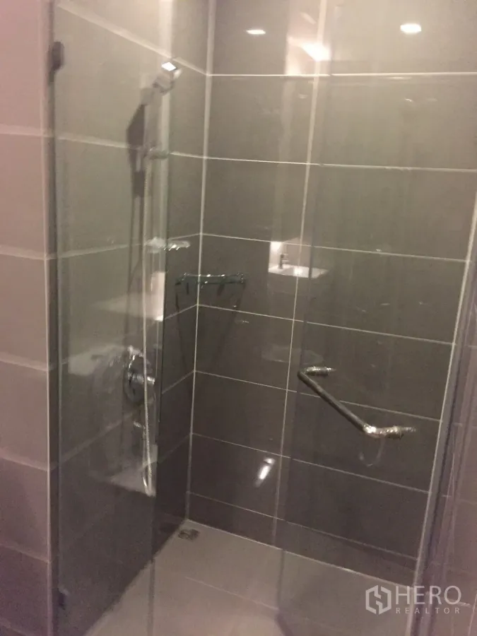 Condominium for rent in Watthana, Bangkok - Modern bathroom with glass-enclosed shower and gray tiled walls.