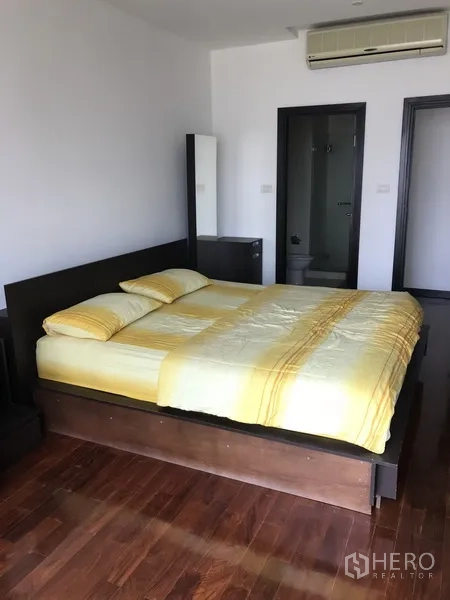 Condominium for rent in Khlong Toei, Bangkok - Master bedroom with wood flooring, double bed, and entrance to an ensuite bathroom.
