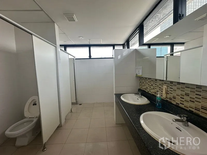 Office Space for rent in Bang Rak, Bangkok - Bright restroom with sinks, stalls and high windows for ventilation.