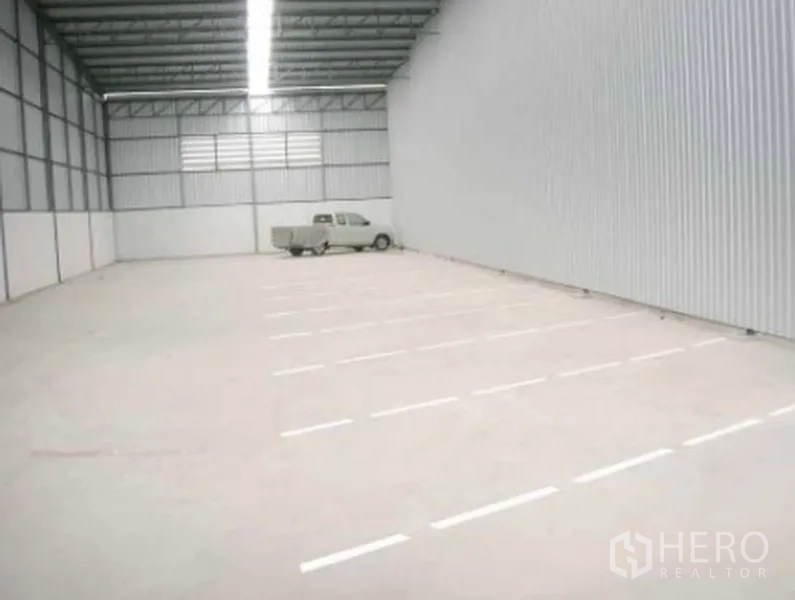 Warehouse for rent in Phra Pradaeng, Samut Prakan - Spacious empty warehouse interior with high metal roof, bright linear lighting and smooth concrete floor.