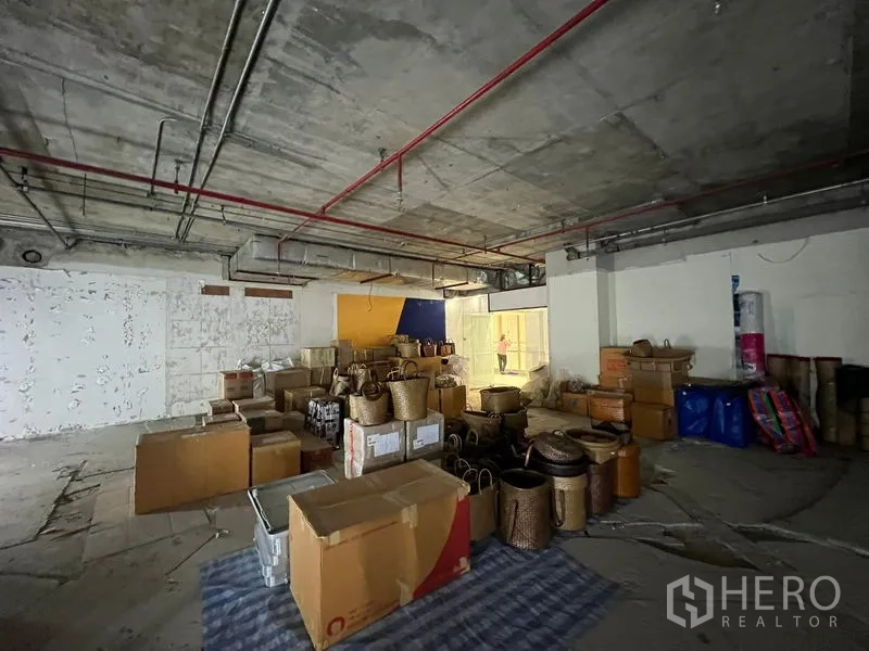 Retail Space for rent - Raw retail unit with concrete ceiling, fire sprinklers and stacked woven baskets and cartons.