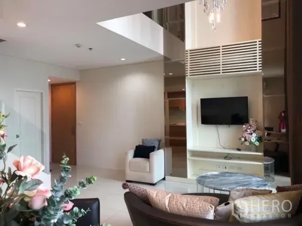 公寓 出租在Ratchathewi, Bangkok - 带电视墙与单人沙发的起居角，镜面与水晶吊灯点缀。