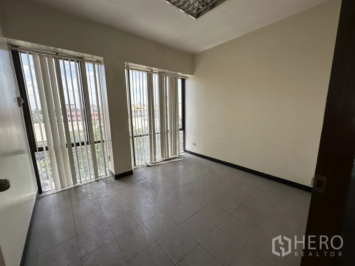 Warehouse for rent in Suan Luang, Bangkok - Compact corner office with tall windows, vertical blinds, and a city outlook.