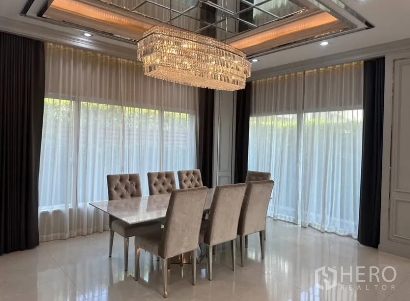Detached House for rent or sale in Prawet, Bangkok - Formal dining room with marble table, six upholstered chairs, and a grand chandelier.
