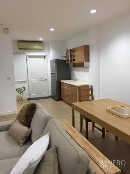 Townhouse for rent in Lat Phrao, Bangkok - Compact kitchen off the living area with wooden cabinets, dining table and refrigerator.