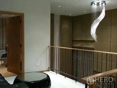 Condominium for rent or sale in Khlong Toei, Bangkok - Loft-style mezzanine with railing and a spiral crystal chandelier.