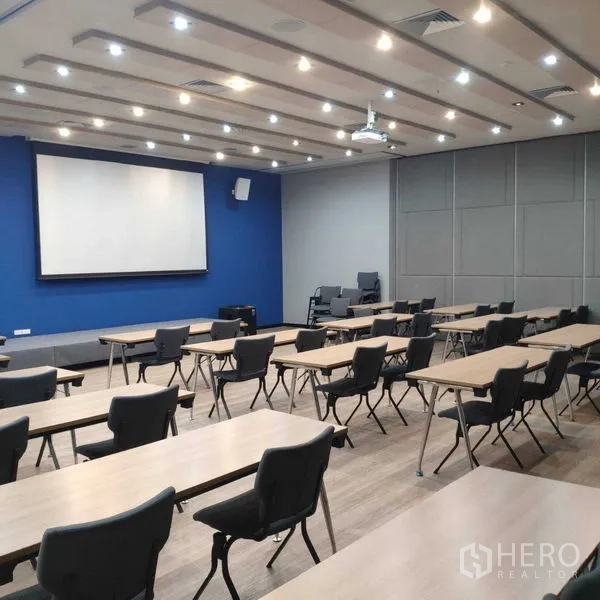 Office Space for rent - Training or seminar room with projector screen and rows of tables and chairs.