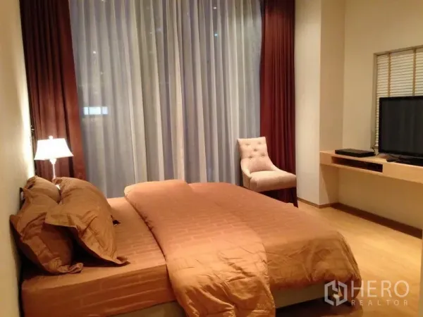 Condominium for sale in Bang Rak, Bangkok - Master bedroom with large bed, sheer and blackout curtains, accent chair and TV.