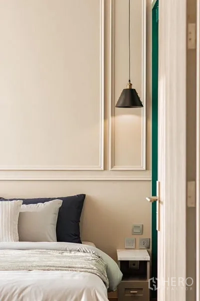 Condominium for rent in Khlong Toei, Bangkok - Bedside scene with classic wall molding, nightstand, and black pendant sconce.