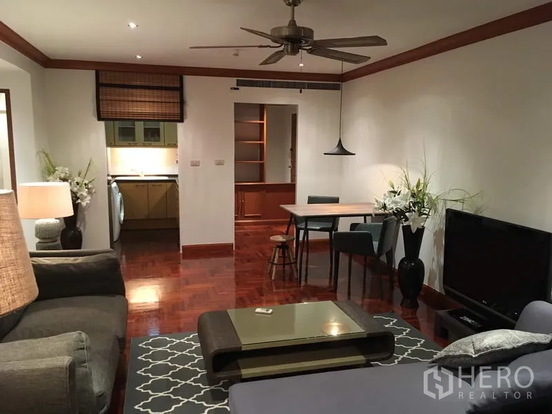 Condominium for rent in Sathon, Bangkok - Open-plan living and dining room with wooden floors, ceiling fan, TV console and a view into the separate kitchen.