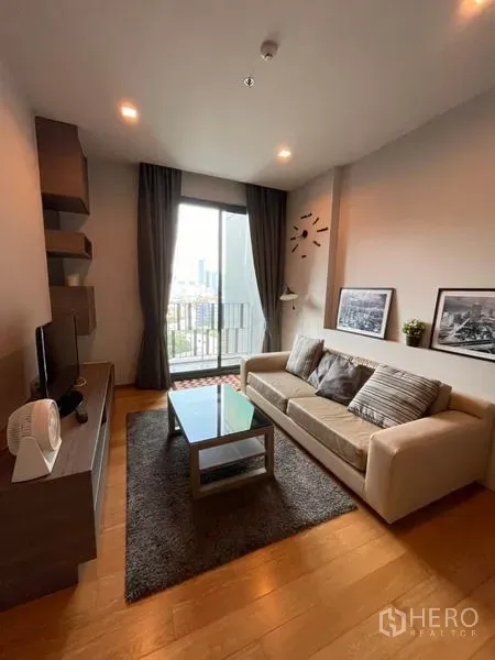 Condominium for rent in Khlong Toei, Bangkok - Cozy living room with sofa, TV console, glass coffee table and balcony city view in a modern Bangkok condo.
