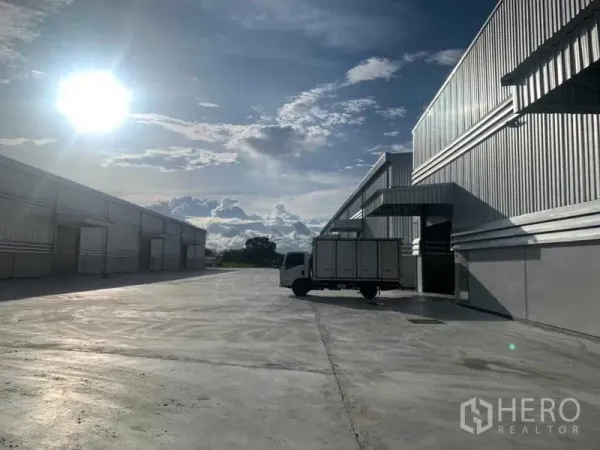 货栈 出租在Ban Bueng, Chon Buri - 货车停靠在仓库装卸区，宽阔混凝土场地沐浴在夕阳下。