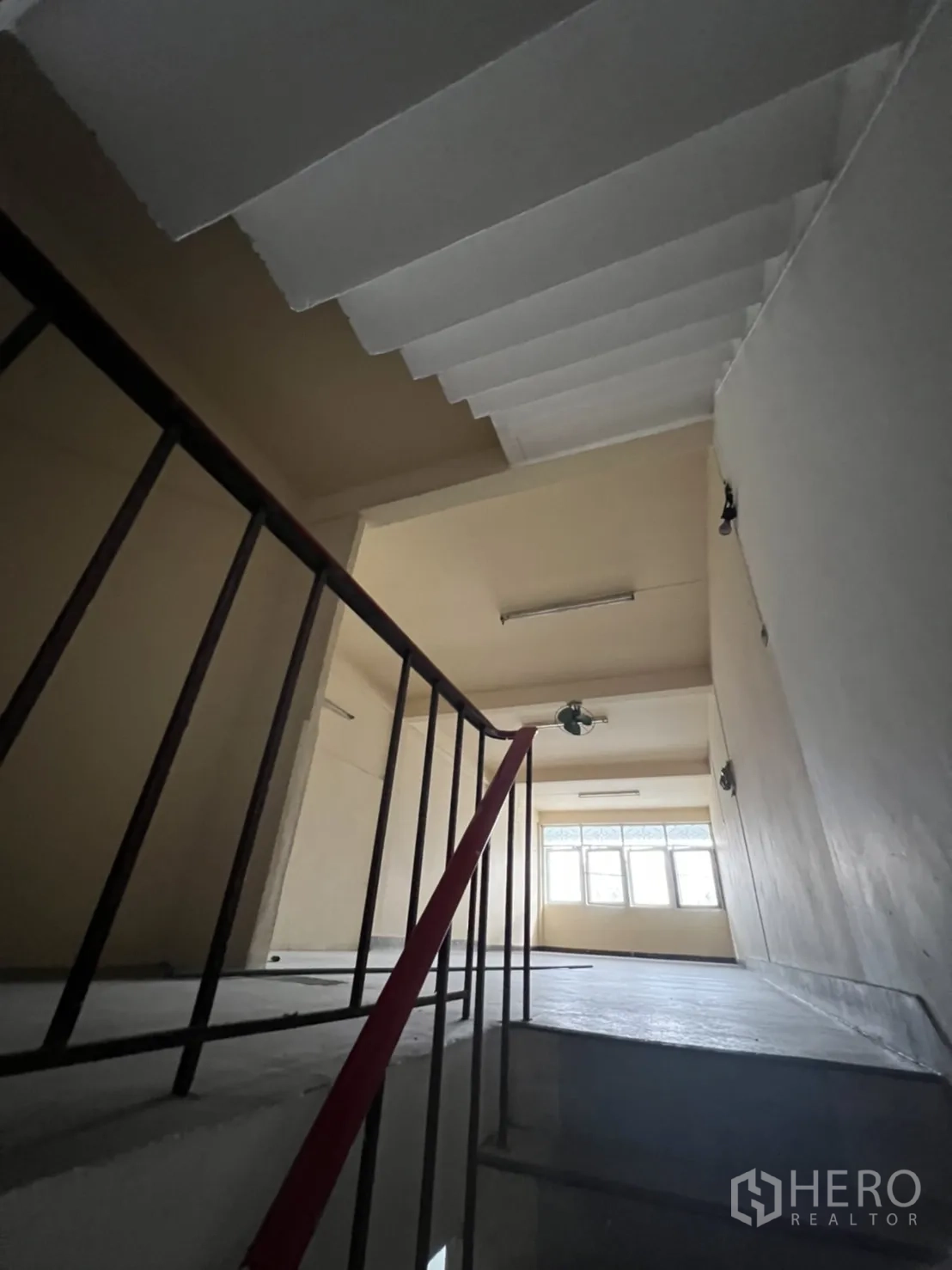 Shophouse for rent in Phra Khanong, Bangkok - Concrete staircase rising to bright upper level with wide window providing natural light.