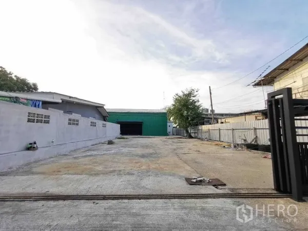 Warehouse for rent in Bang Na, Bangkok - Wide concrete driveway leading to a green metal warehouse and open yard