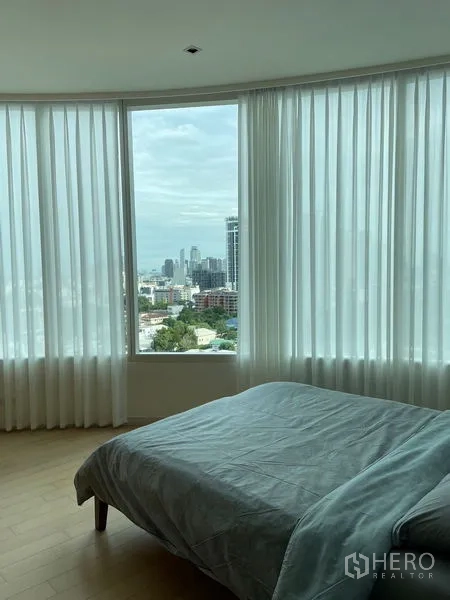 公寓 出租在Watthana, Bangkok - 卧室设落地弧形窗与纱帘，可欣赏城市天际线景观。