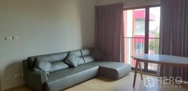 公寓 出租在Watthana, Bangkok - 客厅配灰色转角沙发、圆形餐桌，推拉门通向阳台。