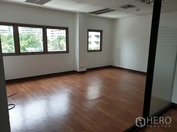 Office Space for rent in Khlong Toei, Bangkok - Corner office room with wood flooring and multiple windows overlooking greenery.