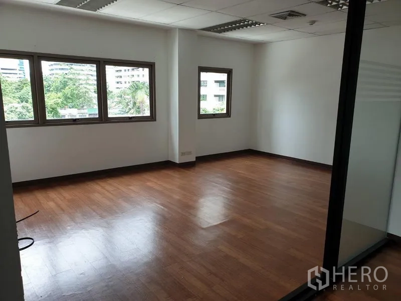 Office Space for rent in Khlong Toei, Bangkok - Corner office room with wood flooring and multiple windows overlooking greenery.