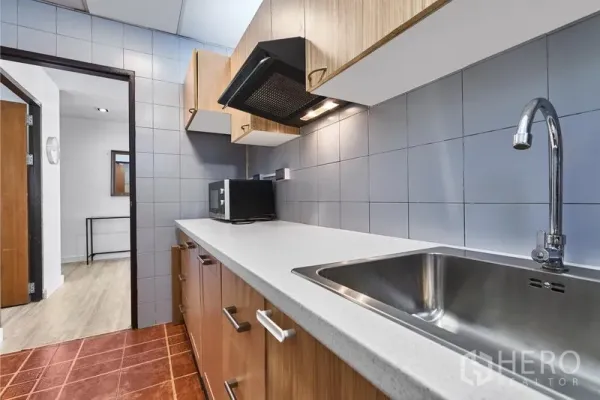 Condominium for rent in Watthana, Bangkok - Galley kitchen with stone countertop, sink, range hood and microwave.