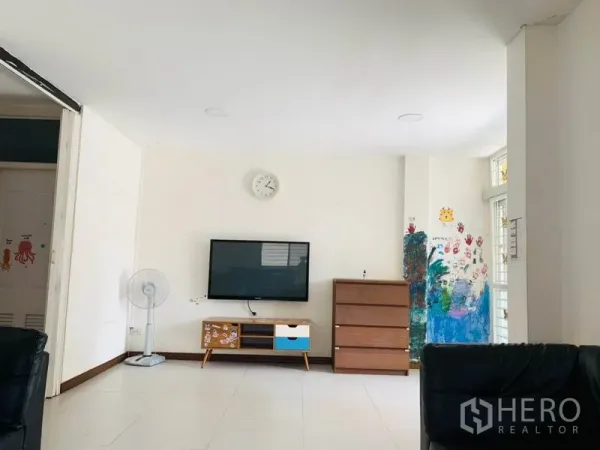 Townhouse for rent or sale in Huai Khwang, Bangkok - Spacious family area with wall-mounted TV, clock, dresser and a large window