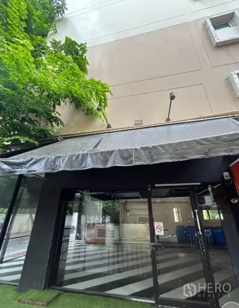 Retail Space for rent in Bang Rak, Bangkok - Close-up of glass entrance with dark awning beneath tree shade.