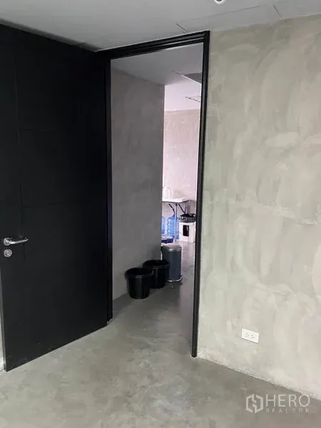 办公空间 出租在Khlong Toei, Bangkok - 通往私密房间的入口，黑色门与质感水泥墙面。