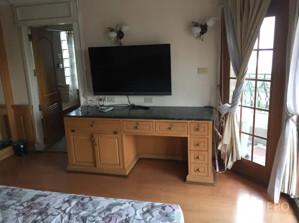Condominium for rent in Khlong Toei, Bangkok - Wall-mounted TV over a wooden desk with French doors and curtains leading to the balcony.
