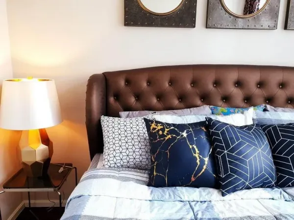 Condominium for rent or sale in Watthana, Bangkok - Cozy bedroom with a tufted headboard, accent cushions and warm bedside lighting.