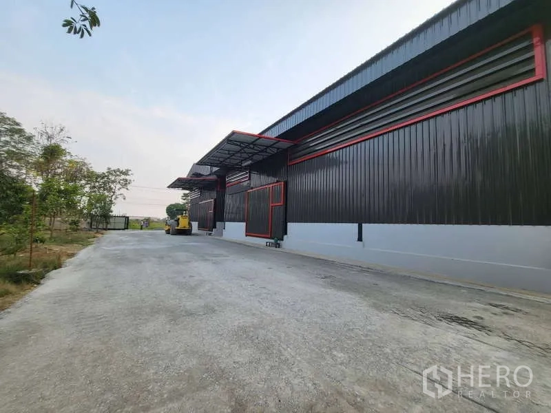 Warehouse for rent in Sam Phran, Nakhon Pathom - Side view of black metal-clad warehouse with loading canopies and a wide truck-friendly driveway.