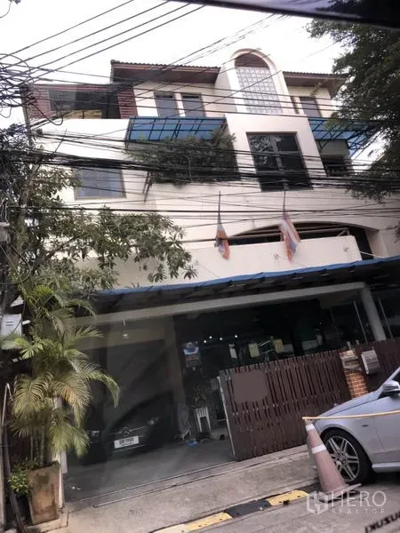 Home Office for sale in Huai Khwang, Bangkok - Multi-storey home office in Huai Khwang, Bangkok with glass awnings, balconies, gated carport, and street trees.