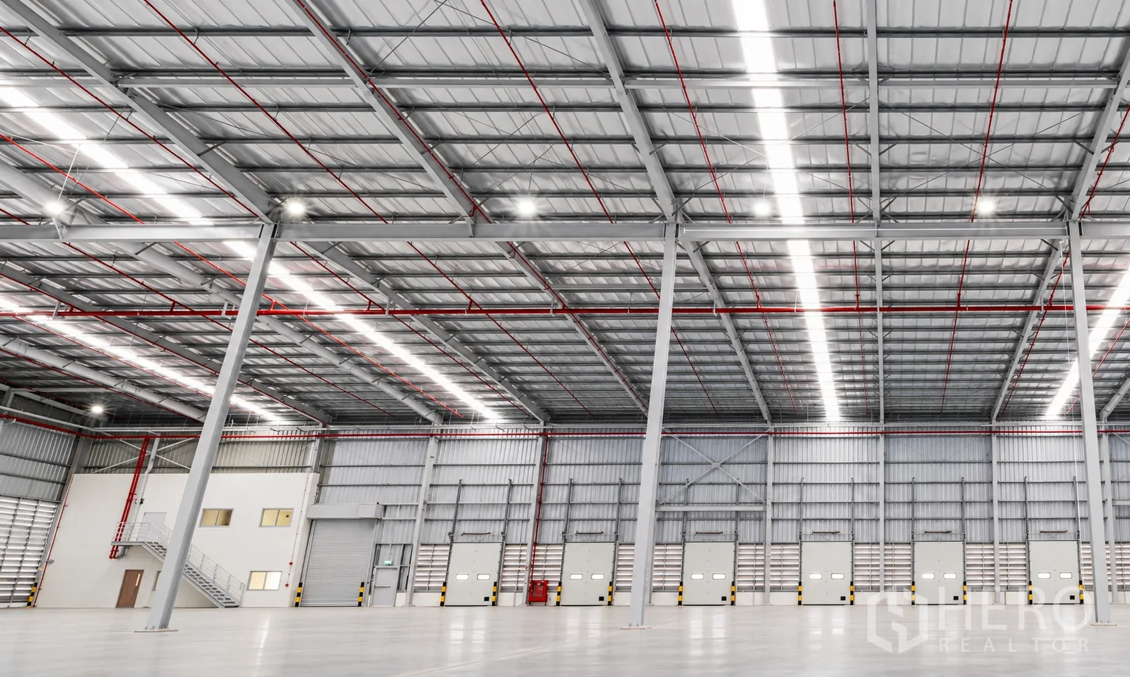 Warehouse for rent in Si Racha, Chon Buri - Large warehouse interior with high steel roof, dock doors, and an internal office unit with stairs.