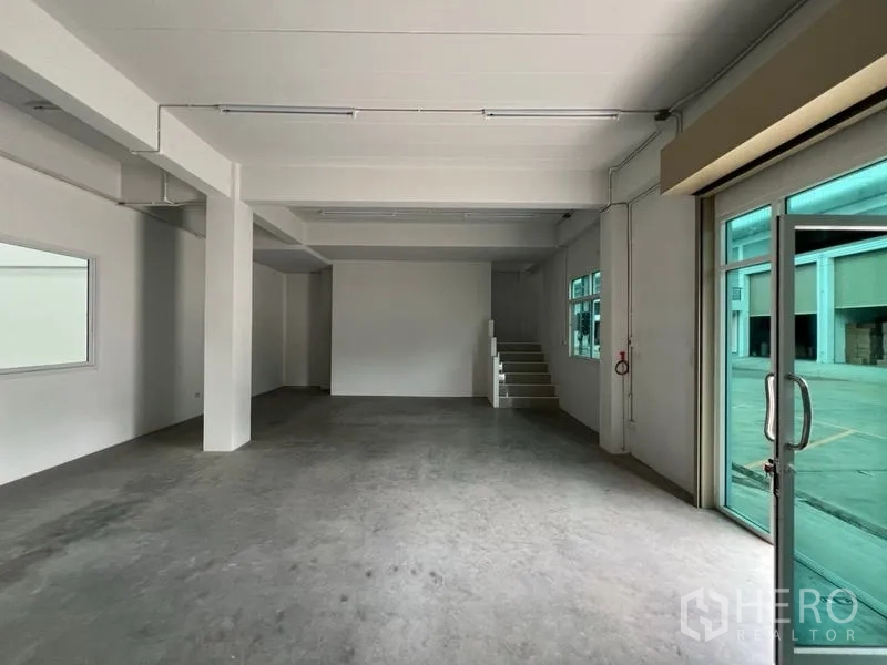 Factory for rent in Phra Samut Chedi, Samut Prakan - Ground-floor reception or workspace with glass entrance, concrete flooring and stairs to the mezzanine.
