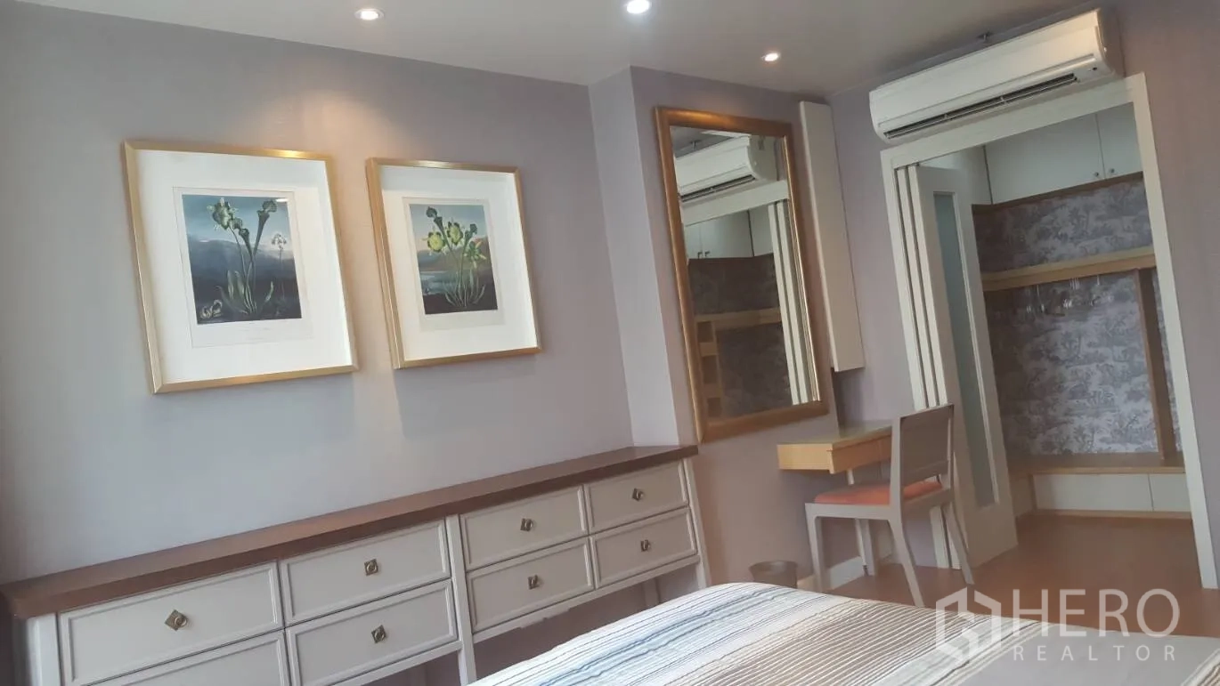 Condominium for rent in Khlong Toei, Bangkok - Wall with framed art, large mirror, dresser and entry to a walk-in closet.