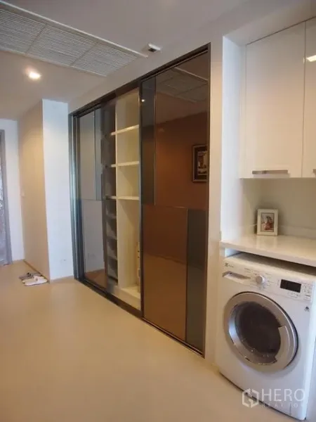 公寓 出售在Watthana, Bangkok - 走廊洗衣区，前置洗衣机、白色橱柜与镜面滑门收纳，现代公寓。