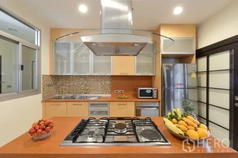 อพาร์ทเมนท์ for rent in Watthana, Bangkok - ครัวสมัยใหม่มีเตาแก๊สบนไอส์แลนด์ เครื่องดูดควัน ผนังกระเบื้องโมเสก และตู้เย็นสแตนเลส