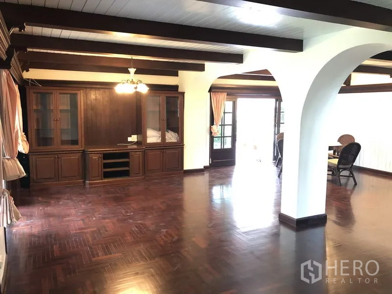Detached House for rent in Khan Na Yao, Bangkok - Spacious living room with dark hardwood floors, exposed ceiling beams, built-in wooden cabinets and French doors.
