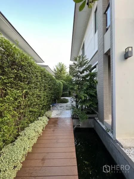 บ้าน ให้เช่าในSuan Luang, Bangkok - ทางเดินแคบข้างบ้านพร้อมสะพานไม้ริมบ่อปลาและแนวพุ่มไม้