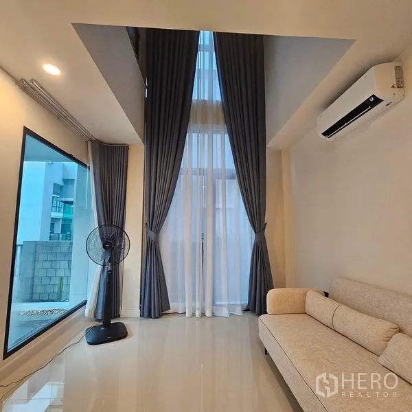 Detached House for rent in Saphan Sung, Bangkok - Cozy lounge with tall windows, high ceiling, sofa and wall-mounted air conditioner.