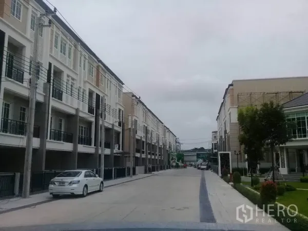 Home Office for rent in Bang Na, Bangkok - Wide internal road lined with new townhome-style offices and parking bays within the community.