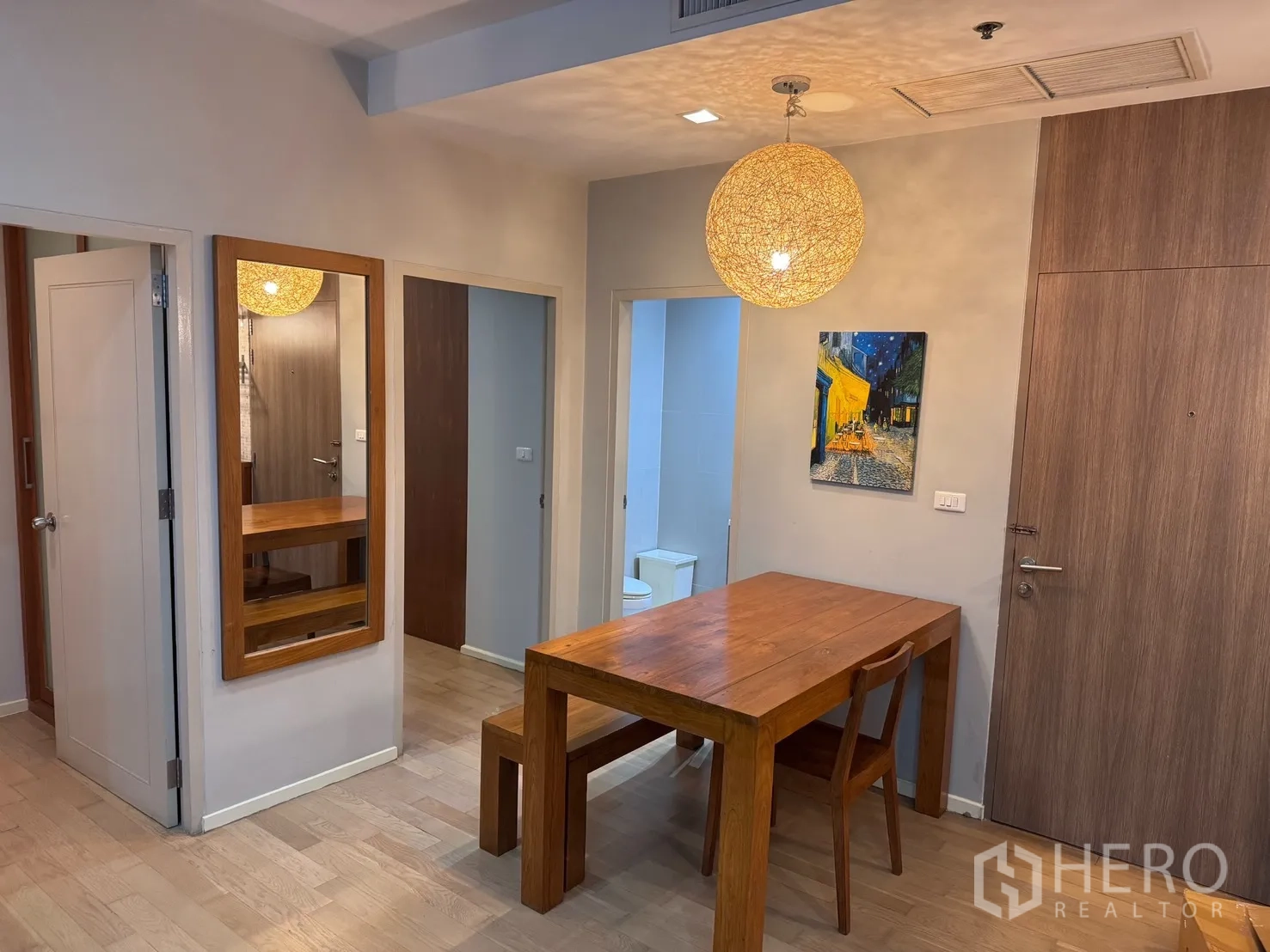 公寓 for rent or sale in Watthana, Bangkok - 用餐区设实木餐桌与长凳，大幅镜面与圆形吊灯增添温馨感，旁有入户门。