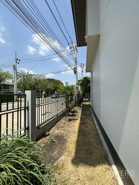Detached House for sale in Lam Luk Ka, Pathum Thani - Side yard along a metal fence beside the quiet street.