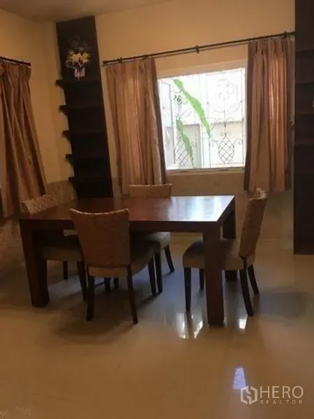 Detached House for rent in Bang Kapi, Bangkok - Dining area with a wooden table, four upholstered chairs and a window with drapes.