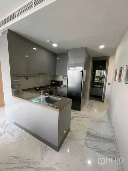 Condominium for rent or sale in Bang Rak, Bangkok - Modern L-shaped kitchen with glossy cabinets, sink, and refrigerator.